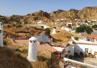 Camini bianchi delle case-grotta emergono dalle colline di tufo rosso di Guadix, Andalusia