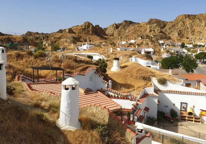 Camini bianchi delle case-grotta emergono dalle colline di tufo rosso di Guadix, Andalusia