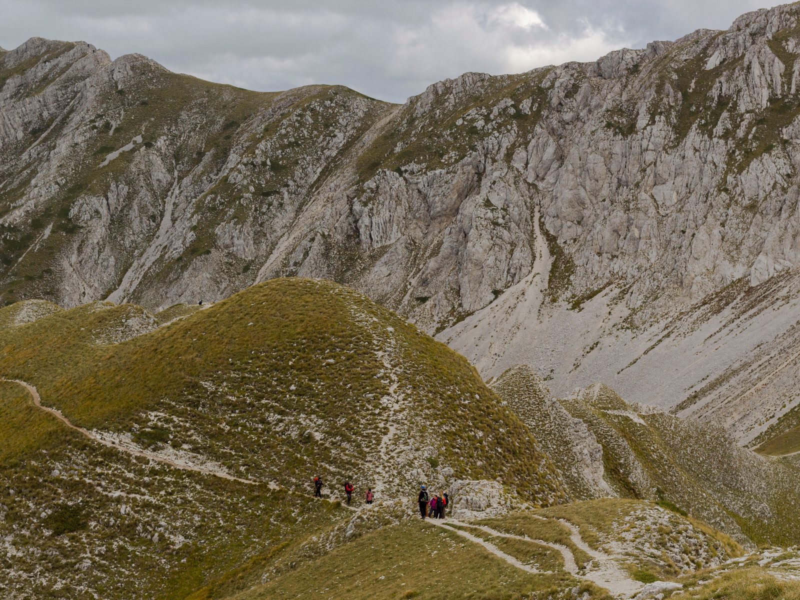 Escursionisti sul sentiero verso il lago di Pilato tra praterie d'alta quota e rocce calcaree